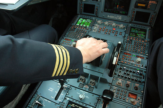 A captain's hand, four gold stripes on the sleeve, on the thrust levers of an airliner flight deck.