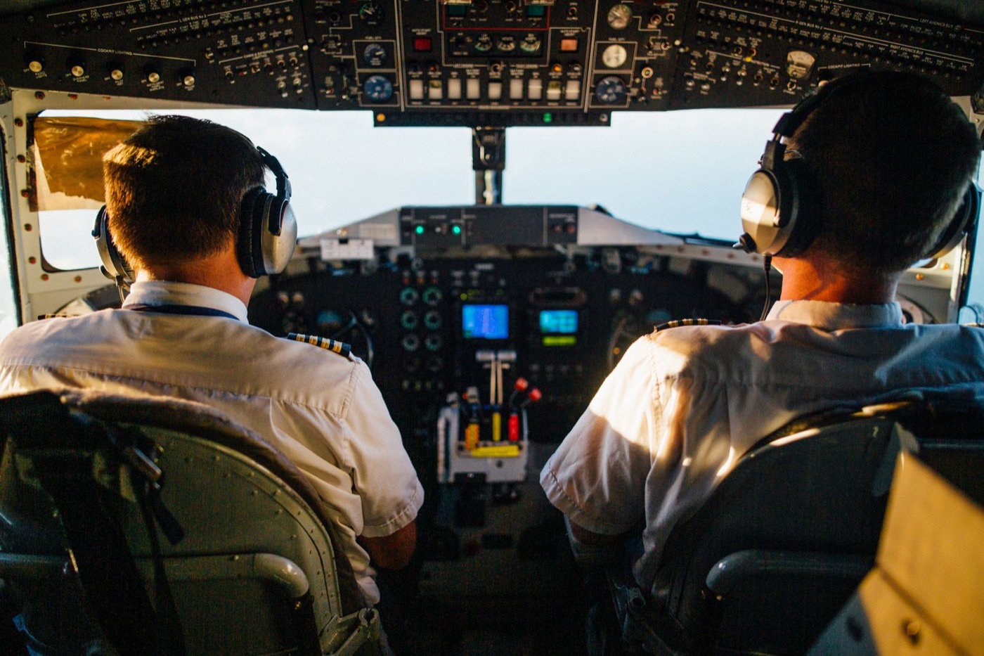 Two pilots working side by side in the cockpit, headsets on, coordinating as a crew.