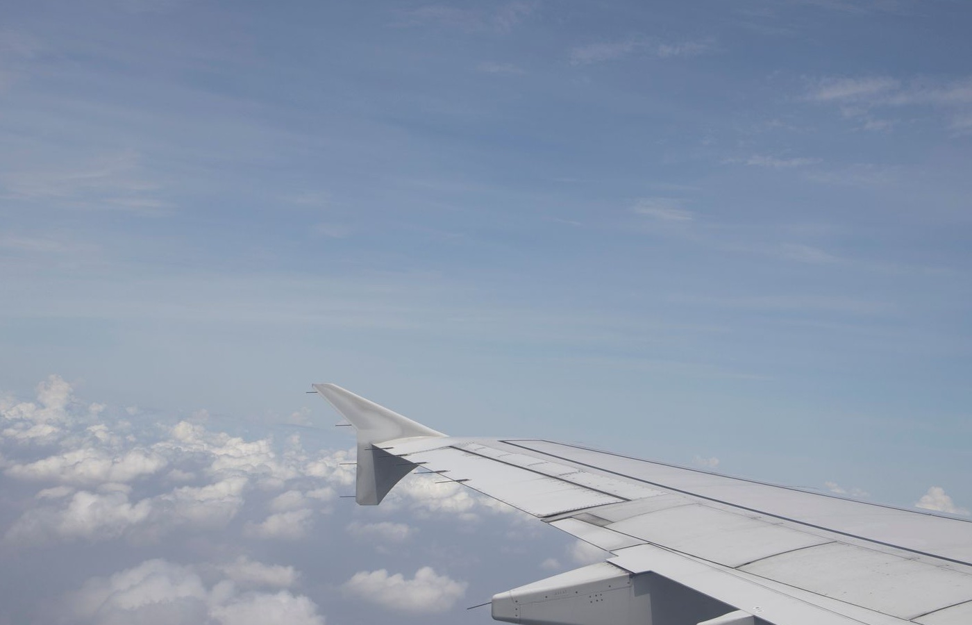 A calm view through an aircraft window, the wing resting over soft white clouds and blue sky.